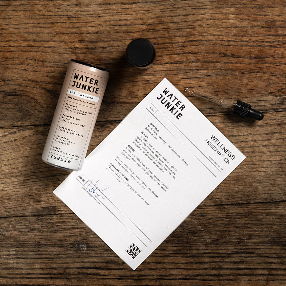 Water Junkie white peach can laying on a wooden table next to a "wellness prescription" document